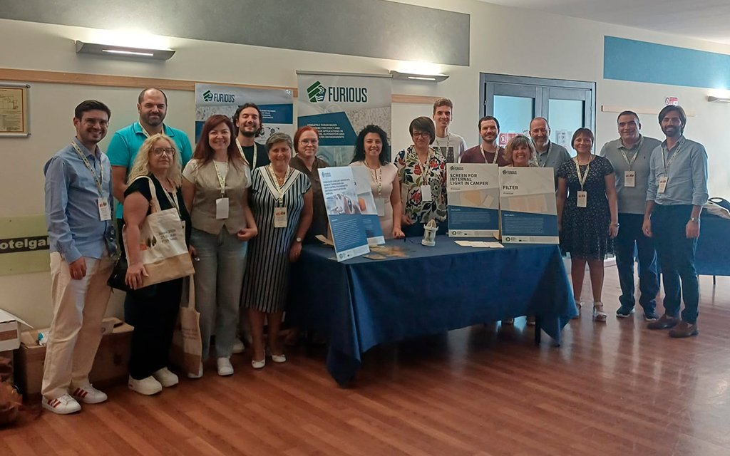 A group of people standing and posing at a scientific conference. In front of them, in the centre, is a table displaying the posters and prototypes that were shown at the conference.
