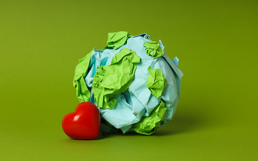 Representation of the Earth made of blue and green paper, with a red heart beside it on a green background.